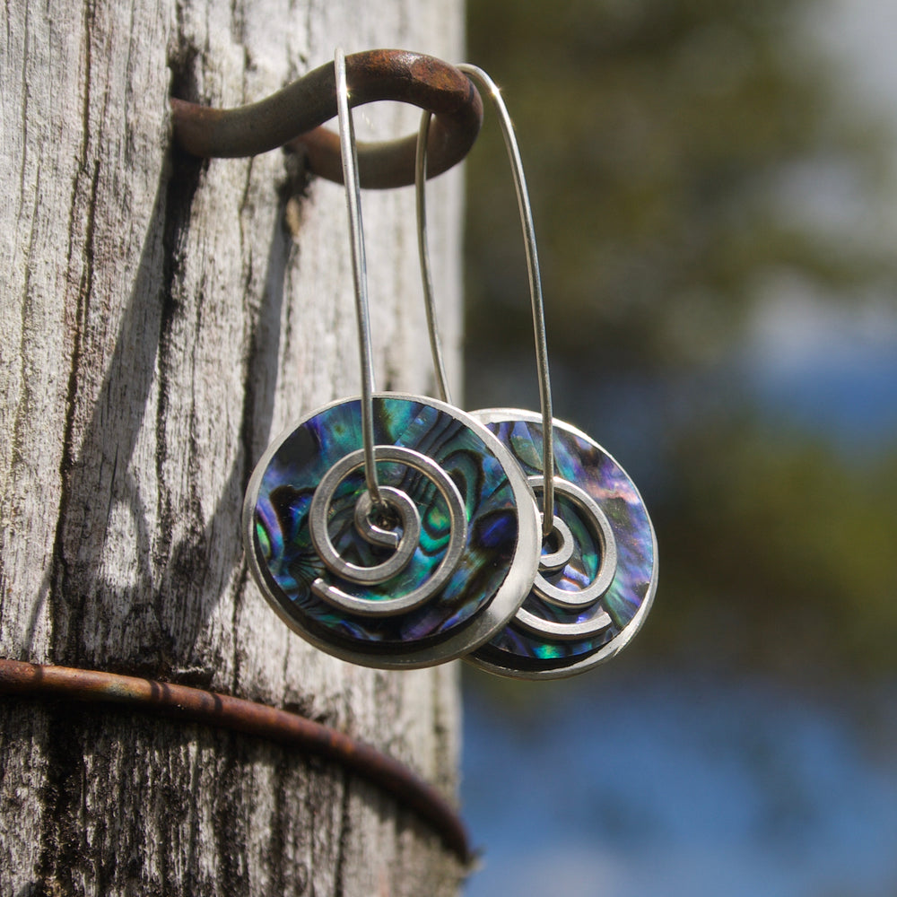 Silver Pāua Spiral Drops Earrings on rustic fence post